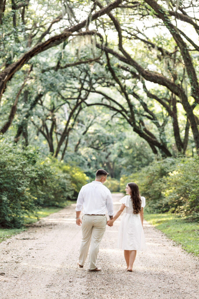 A couple dressed in white walking in front of lush greenery at their Afton Villa Gardens engagement session