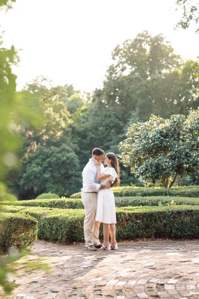 A couple dressed in white kissing in the lush garden greenery at their Afton Villa Gardens engagement session