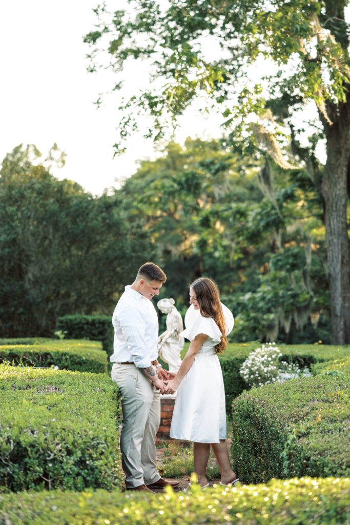 A couple dressed in white holding hands in the lush garden greenery at their Afton Villa Gardens engagement session