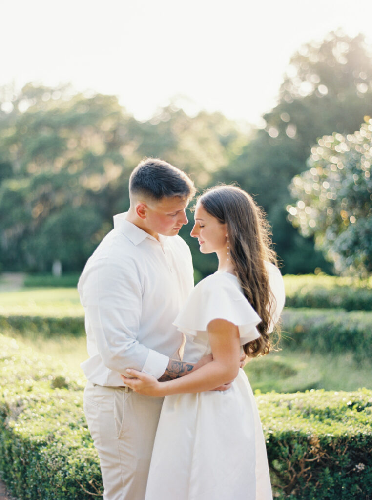 A couple dressed in white in front of greenery at their Afton Villa Gardens engagement session