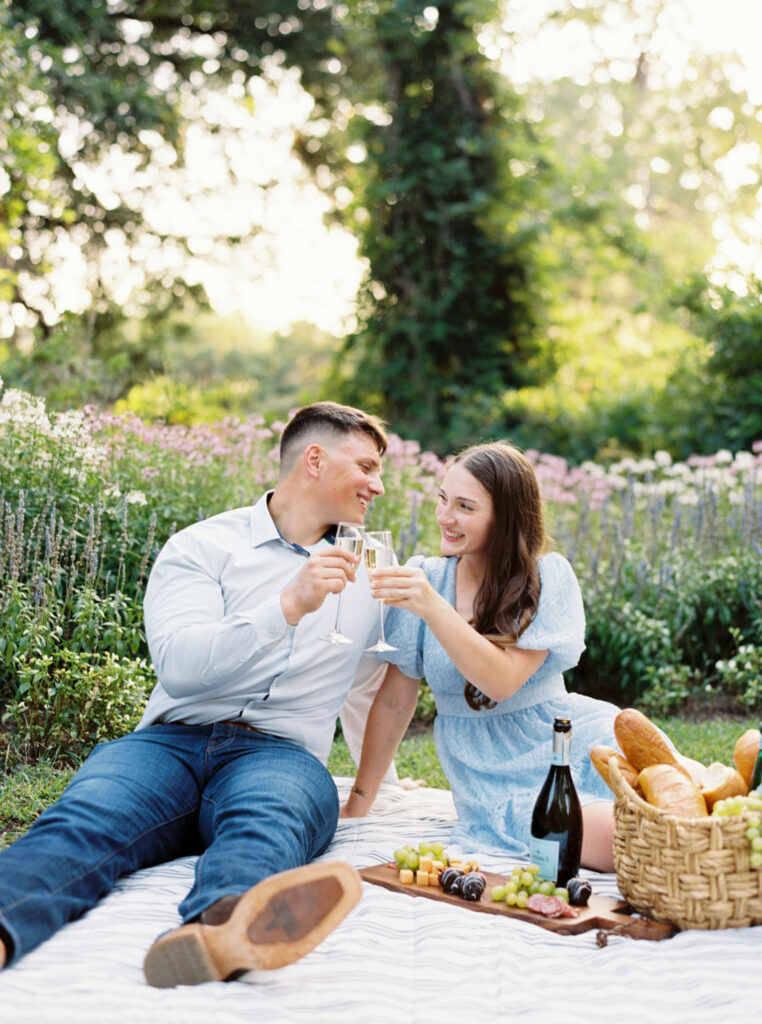 A couple dressed in soft blues having a picnic on the grass at their Afton Villa Gardens engagement session