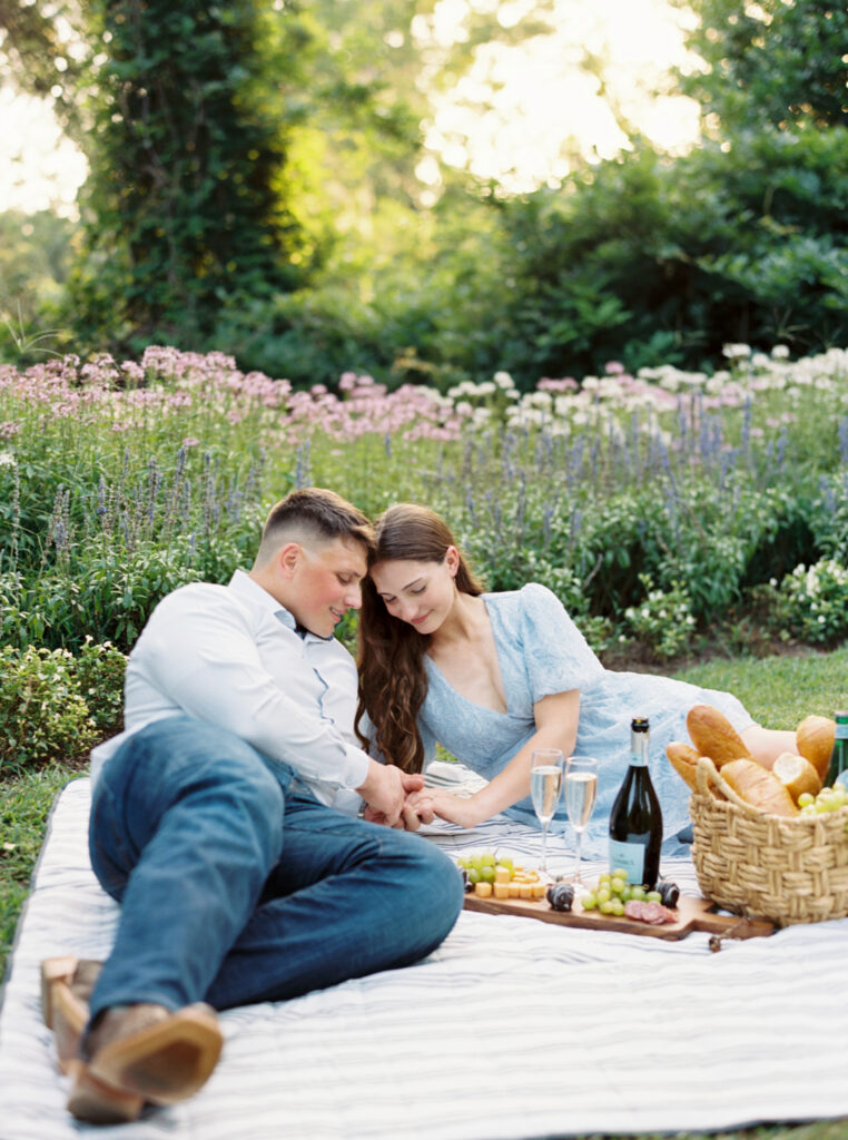 A couple dressed in soft blues having a picnic on the grass at their Afton Villa Gardens engagement session