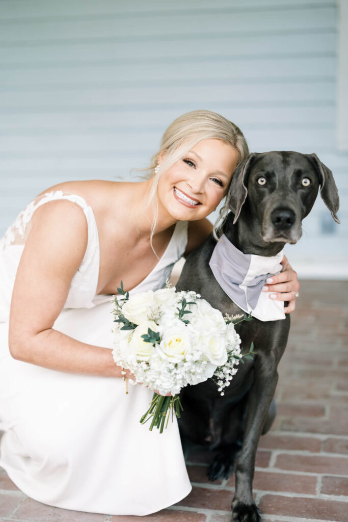 A bridal portrait at John Nickerson House in Lafayette, LA, showing a smiling bride in a white gown holding a bouquet with a black dog.