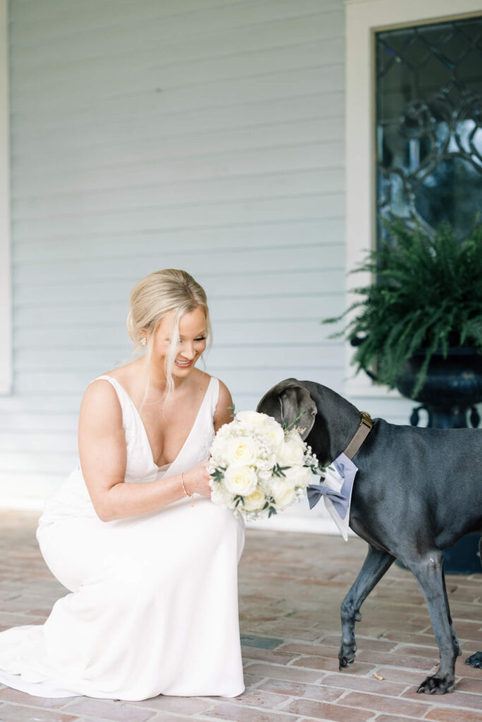 A bridal portrait at John Nickerson House in Lafayette, LA, showing a smiling bride in a white gown holding a bouquet with a black dog.