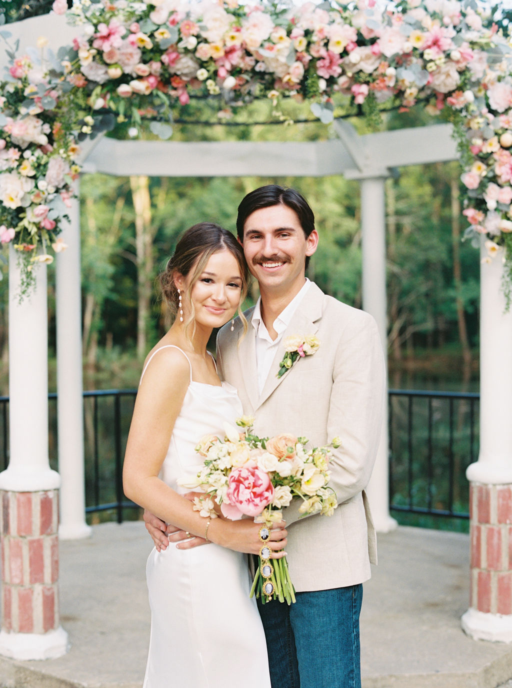 A bride in white holding a bouquet with her groom in a khaki suit jacket and jeans at Springs Ballroom in Iota, Louisiana.