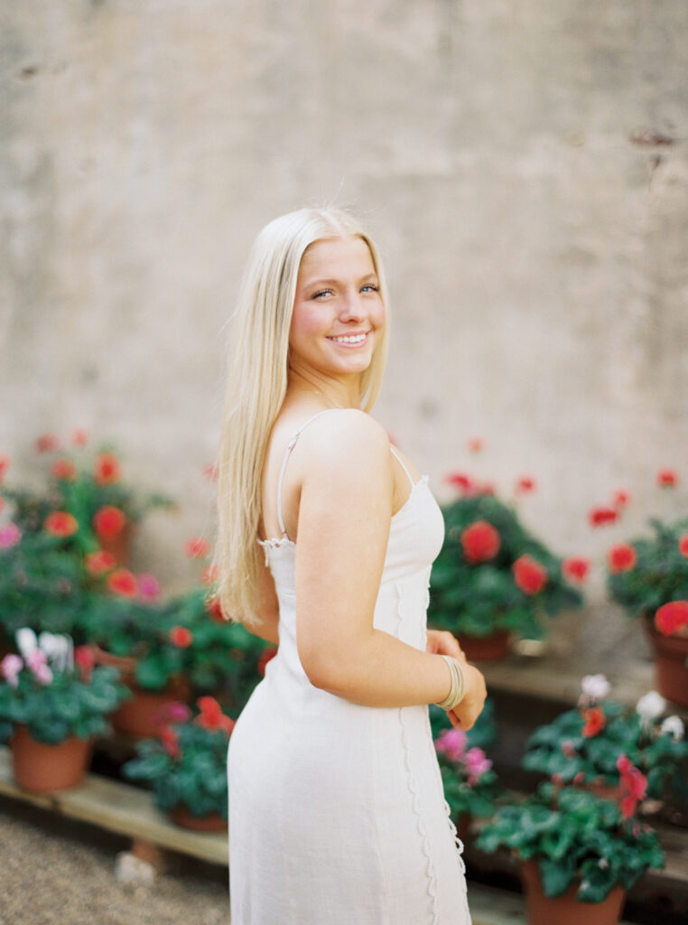 Amy posing infront of the vibrant flower filled greenhouse at Rosedown Plantation during her senior session at Rosedown Plantation, photographed by Morgan Alysse Photography