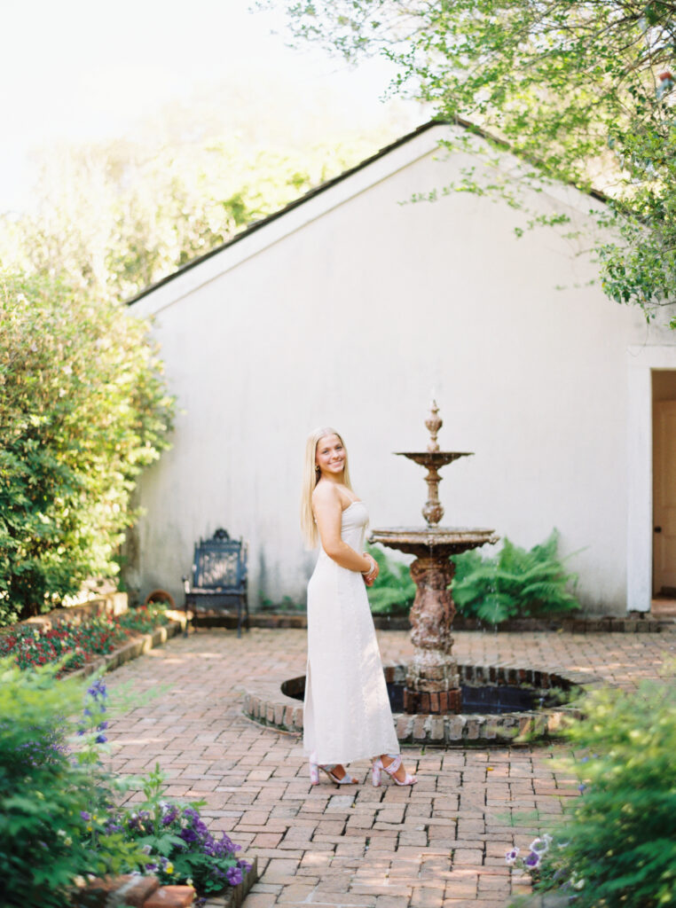 Amy standing in front of a water fountain and cottage hhouse Rosedown Plantation during her senior session at Rosedown Plantation, photographed by Morgan Alysse Photography