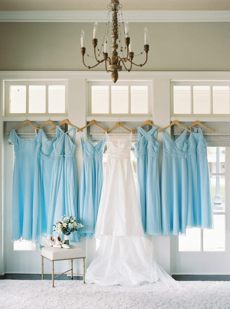 Bridal gown and dusty blue bridesmaid dresses hanging up before Olivia and Landon's Oak Crossing Wedding in Lake Charles, LA, photographed by Morgan Alysse Photography.