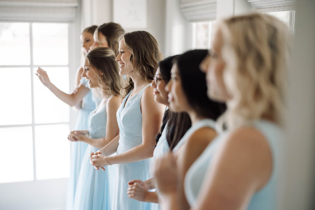 Candid portrait of bride and bridesmaids looking in the mirror in the bridal suite at Olivia and Landon's Oak Crossing Wedding in Lake Charles, LA, photographed by Morgan Alysse Photography.