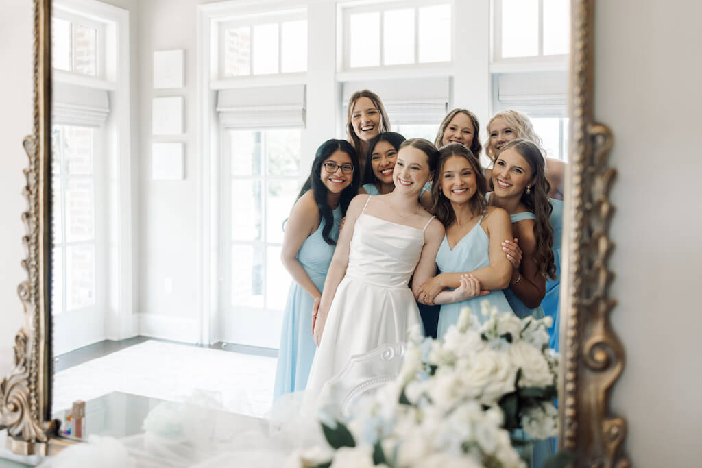 Candid portrait of bride and bridesmaids looking in the mirror in the bridal suite at Olivia and Landon's Oak Crossing Wedding in Lake Charles, LA, photographed by Morgan Alysse Photography.