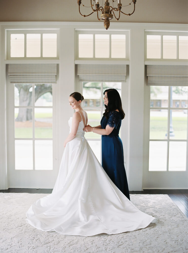 Bride  with her mom butting her dress in the bridal suite at Olivia and Landon's Oak Crossing Wedding in Lake Charles, LA, photographed by Morgan Alysse Photography.