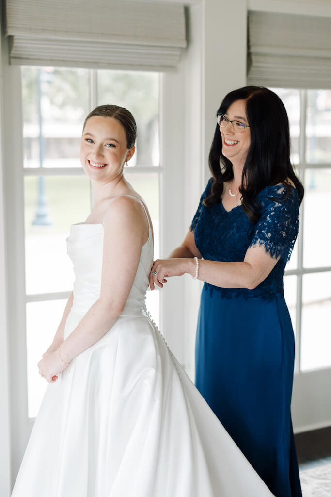 Bride  with her mom butting her dress in the bridal suite at Olivia and Landon's Oak Crossing Wedding in Lake Charles, LA, photographed by Morgan Alysse Photography.