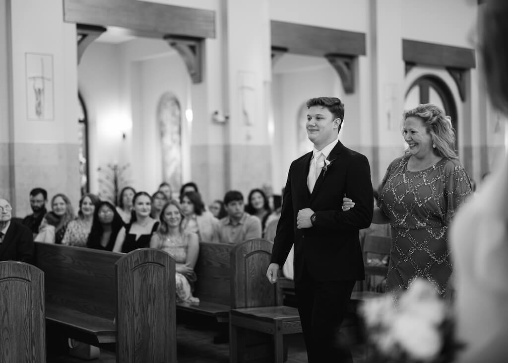 Groom walking down the aisle with his mom at St. Martin De Porres Catholic Church in Lake Charles, Louisiana, on Olivia and Landons Oak Crossing Wedding Day, photographed by Morgan Alysse Photography.