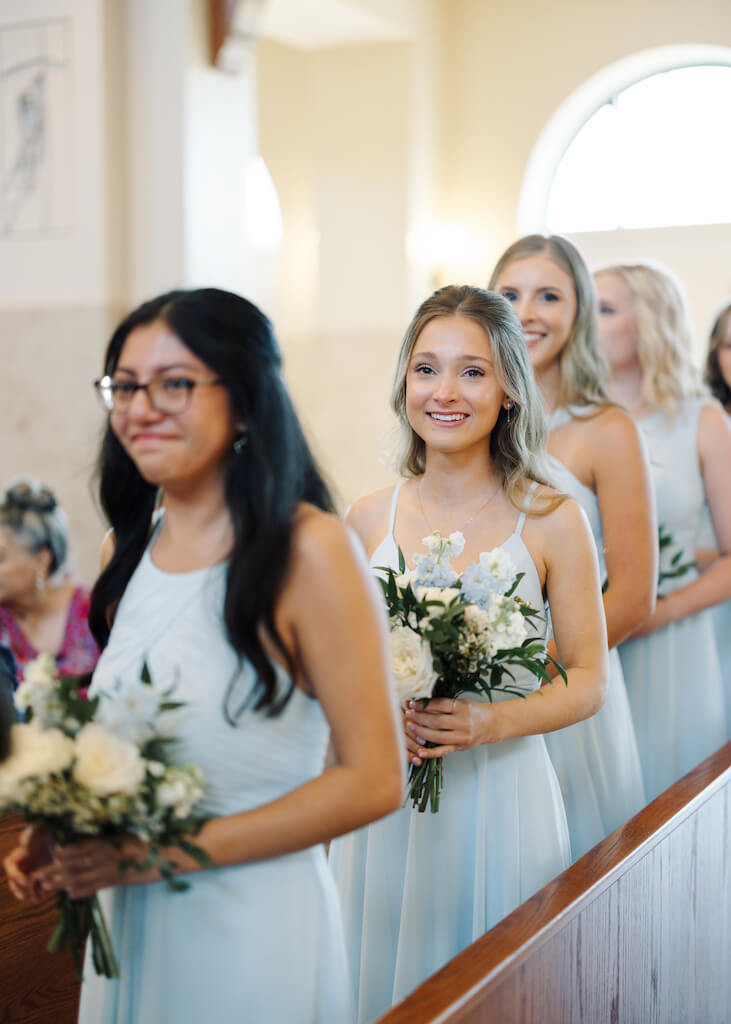 Bridesmaids watching the bride walk down the aisle at St. Martin De Porres Catholic Church in Lake Charles, Louisiana, on Olivia and Landons Oak Crossing Wedding Day, photographed by Morgan Alysse Photography.