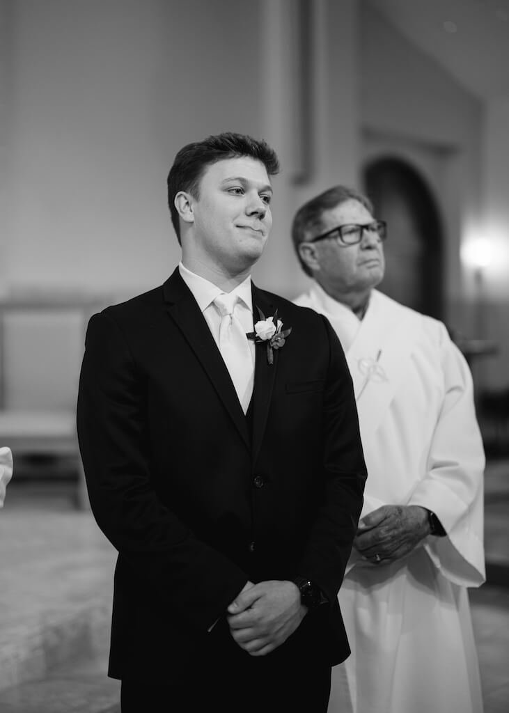 Groom watching the bride walk down the aisle at St. Martin De Porres Catholic Church in Lake Charles, Louisiana, on Olivia and Landons Oak Crossing Wedding Day, photographed by Morgan Alysse Photography.