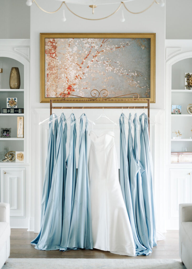 Bridal gown and dusty blue bridesmaid dresses hanging up before Lauren and Colby's rainy day wedding at The Madison in Broussard, LA, photographed by Morgan Alysse Photography.