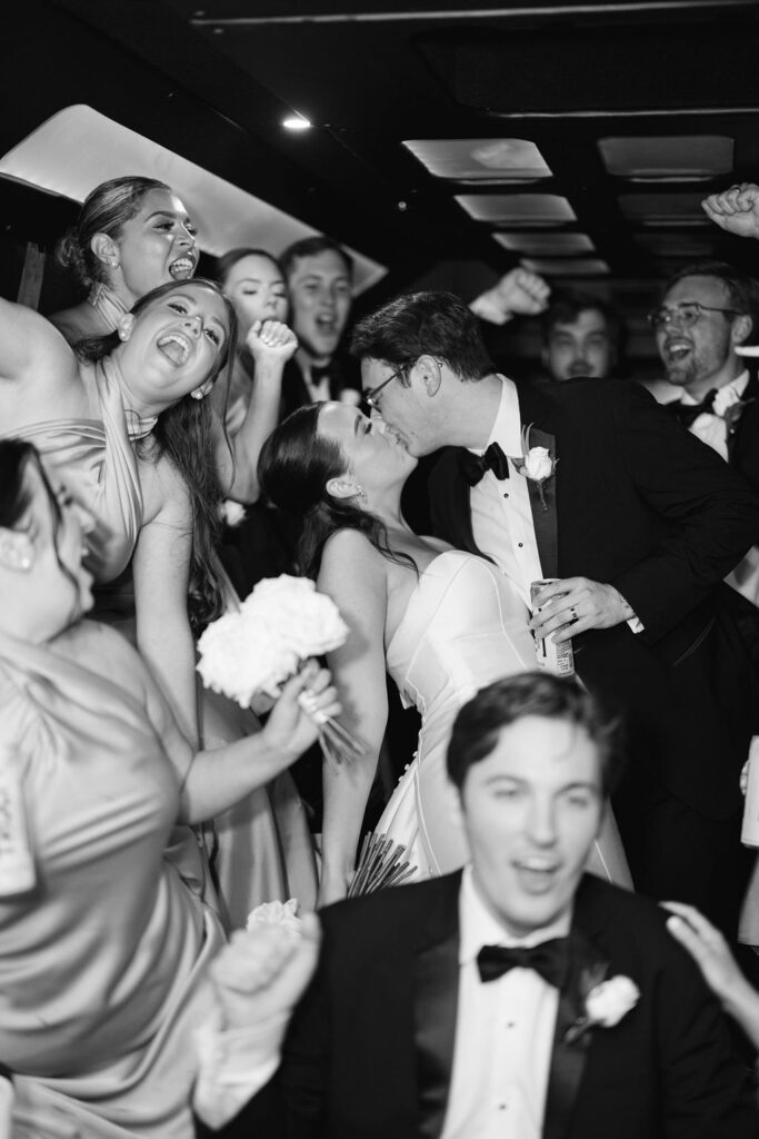 Black and white photo of couple kissing surrounded by friends at Lauren and Colby's rainy day wedding at The Madison in Broussard, LA, photographed by Morgan Alysse Photography.