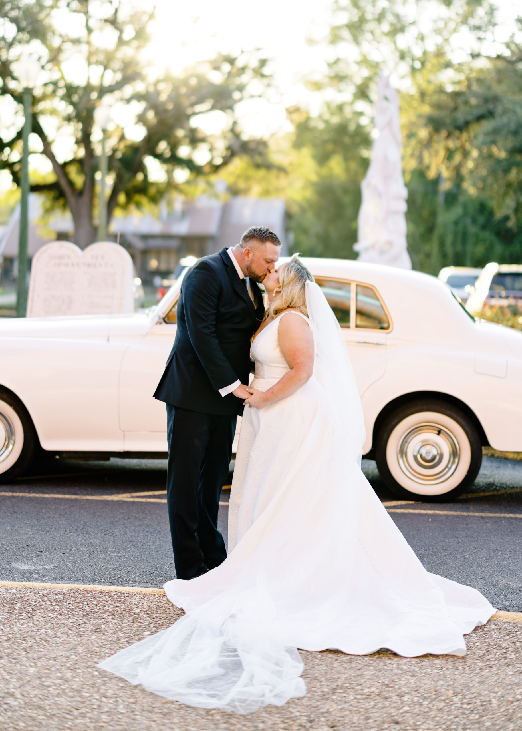 Bride and groom kiss in front of a Rolls Royce at their Opelousas wedding with photos taken by Morgan Alysse Photography