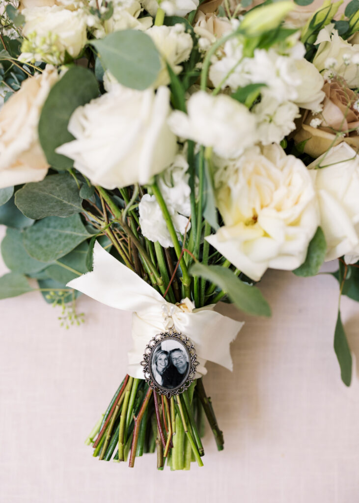 Bridal bouquet with white flowers and a memorial locket with a photo of the bride's father in a wedding details shot by Morgan Alysse Photography