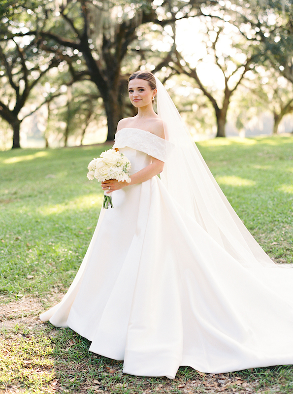 Bride elegantly adjusting her veil on the steps of a historic Louisiana plantation.